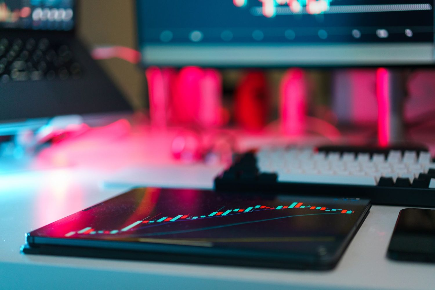 A tablet and monitors showing live charts in a low-lit workspace